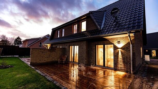 Une maison à deux étages avec une terrasse en bois, des murs en briques et une antenne parabolique.