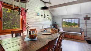 A rustic wooden interior with a dining table, chairs, a bench, and a view through a window.