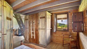 A wooden cabin with a loft bedroom, a wooden chair, and a window with a view.