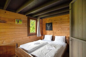 Una cabaña con dos camas de madera, una ventana con cortina y un cuadro de un ciervo en la pared.