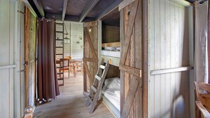 Une pièce rustique en bois, avec un lit superposé, une échelle et un coin repas comprenant une table et des chaises.