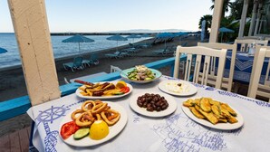 A table with various dishes, a view of the beach, and beach chairs. - Villa Thalia Katerina (Kefalonia)