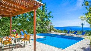 A swimming pool with lounge chairs, a covered patio area, and a table with chairs. - Villa Thalia Katerina (Kefalonia)