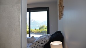 Ein Schlafzimmer mit einem Bett, einer Nachttischlampe und Bergblick durch ein großes Fenster.