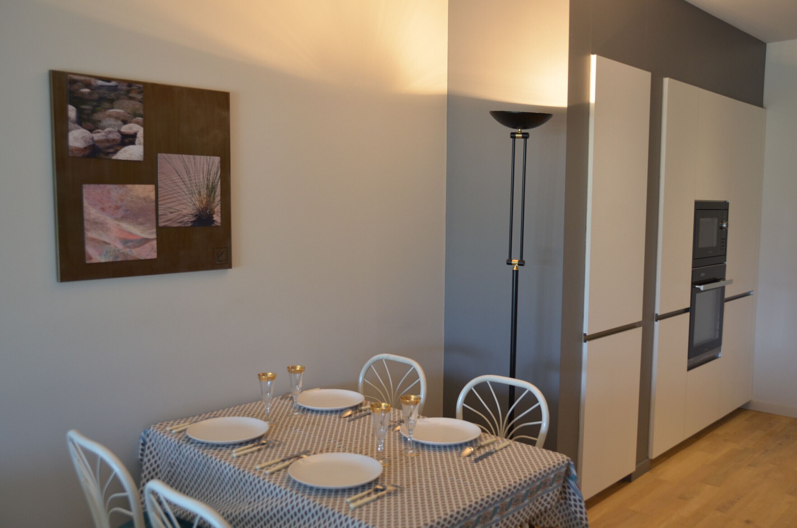 Un coin repas avec une table dressée pour quatre personnes, un lampadaire et un réfrigérateur.