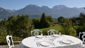 Ein runder Esstisch mit weißen Stühlen, mit Blick auf eine Berglandschaft und einen See.