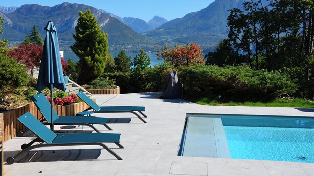 Ein Poolbereich mit Liegestühlen und Sonnenschirm, umgeben von Bergen und Bäumen.