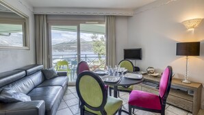 A modern hotel room with a leather sofa, dining table with chairs, a TV, and a balcony with a view of the hills. - La plage privée du lac (Duingt)