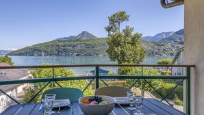 A table with a bowl of fruit and glasses, overlooking a lake and mountains. - La plage privée du lac (Duingt)