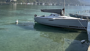 Un voilier est amarré dans une marina, avec une eau claire et des montagnes en arrière-plan.