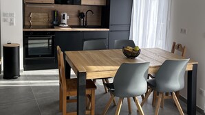 Une cuisine moderne avec des meubles de couleur sombre, une table à manger en bois et un luminaire suspendu noir.