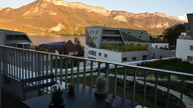 Un balcon avec une table, une véranda et une vue sur une montagne et un lac.