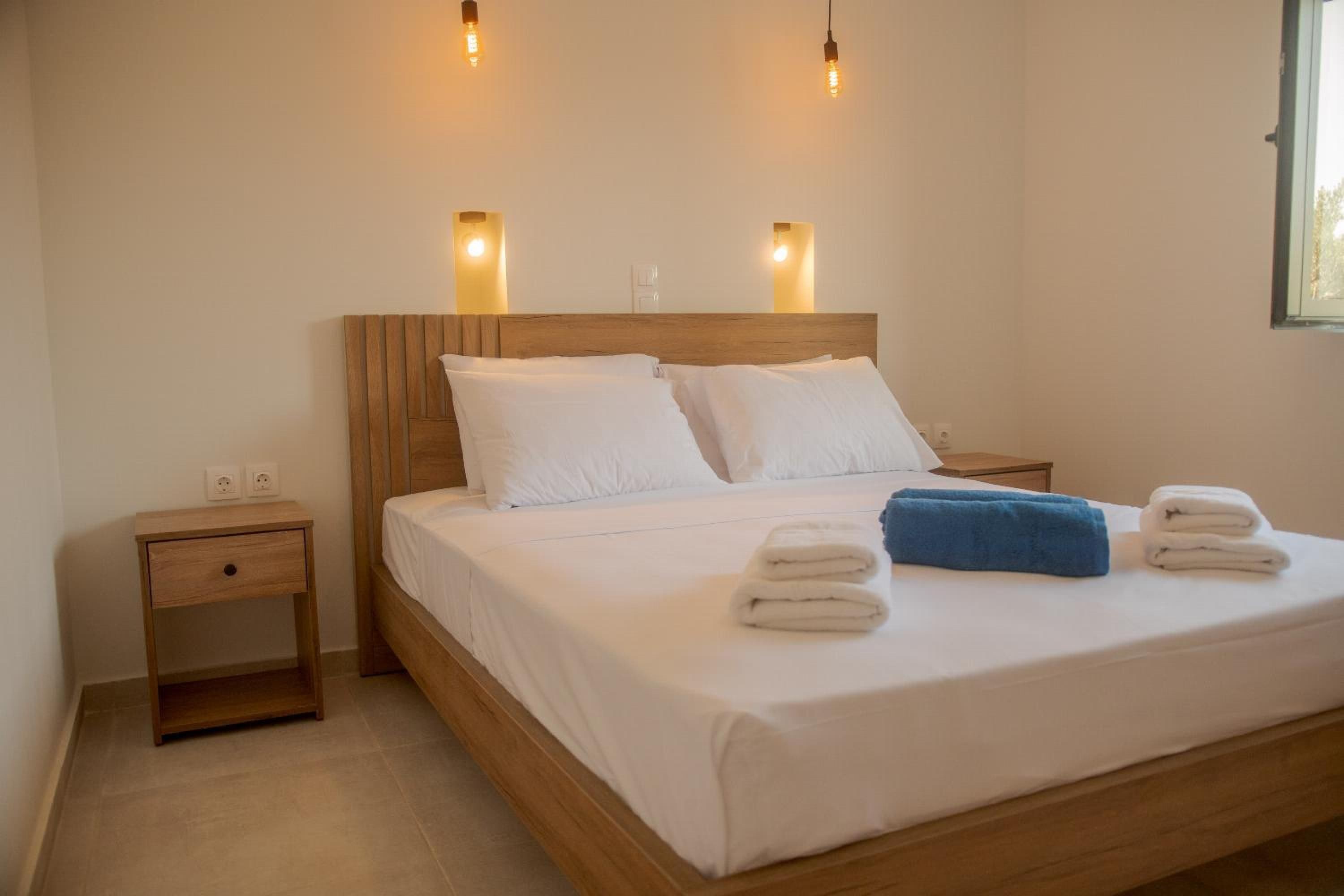A neatly made bed with white linens and two pillows, a wooden nightstand with a drawer, and two wall-mounted light fixtures.