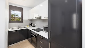 Una cocina moderna con armarios oscuros, encimeras blancas, un microondas y una ventana con vistas al verdor.