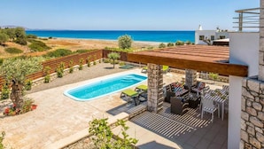Piscina en la azotea con vistas al mar, mobiliario exterior y una pared de piedra.
