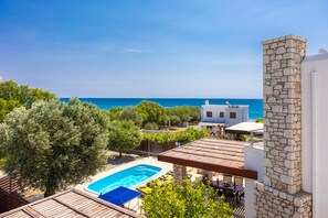 A pool with a view of the sea, a stone tower, and a white building with a balcony. - Villa Ira in Rhodes With 2 Bedrooms and 2 Bathrooms (Rhodes)
