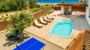 Un espace piscine avec des chaises longues, une table de ping-pong et une vue sur la mer.