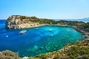 A coastal area with clear turquoise waters, rocky terrain, and boats. - Villa Mediterranean Blue (Rhodes)