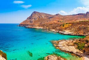 Eine Küstenlandschaft mit klarem türkisblauem Wasser, felsigem Gelände und einem markanten Berg im Hintergrund.
