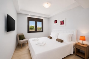 A hotel room with a bed, a chair, a bedside table with a lamp, a TV mounted on the wall, and two framed pictures. - Villa Dionysos in Rhodes (Rhodes)