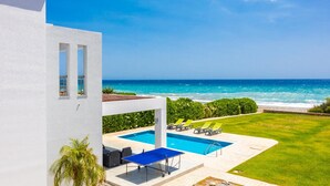 A modern building with a pool, lounge chairs, and a view of the ocean.