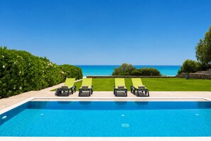 A swimming pool with lounge chairs facing the ocean.