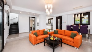 A modern living room with a sectional sofa, a coffee table, and a dining area with purple chairs.