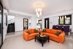 A modern living room with a sectional sofa, a coffee table, and a dining area with purple chairs. - Villa Dionysos in Rhodes (Rhodes)