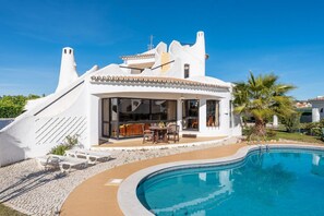 A modern villa with a swimming pool, outdoor seating, and a unique architectural design.