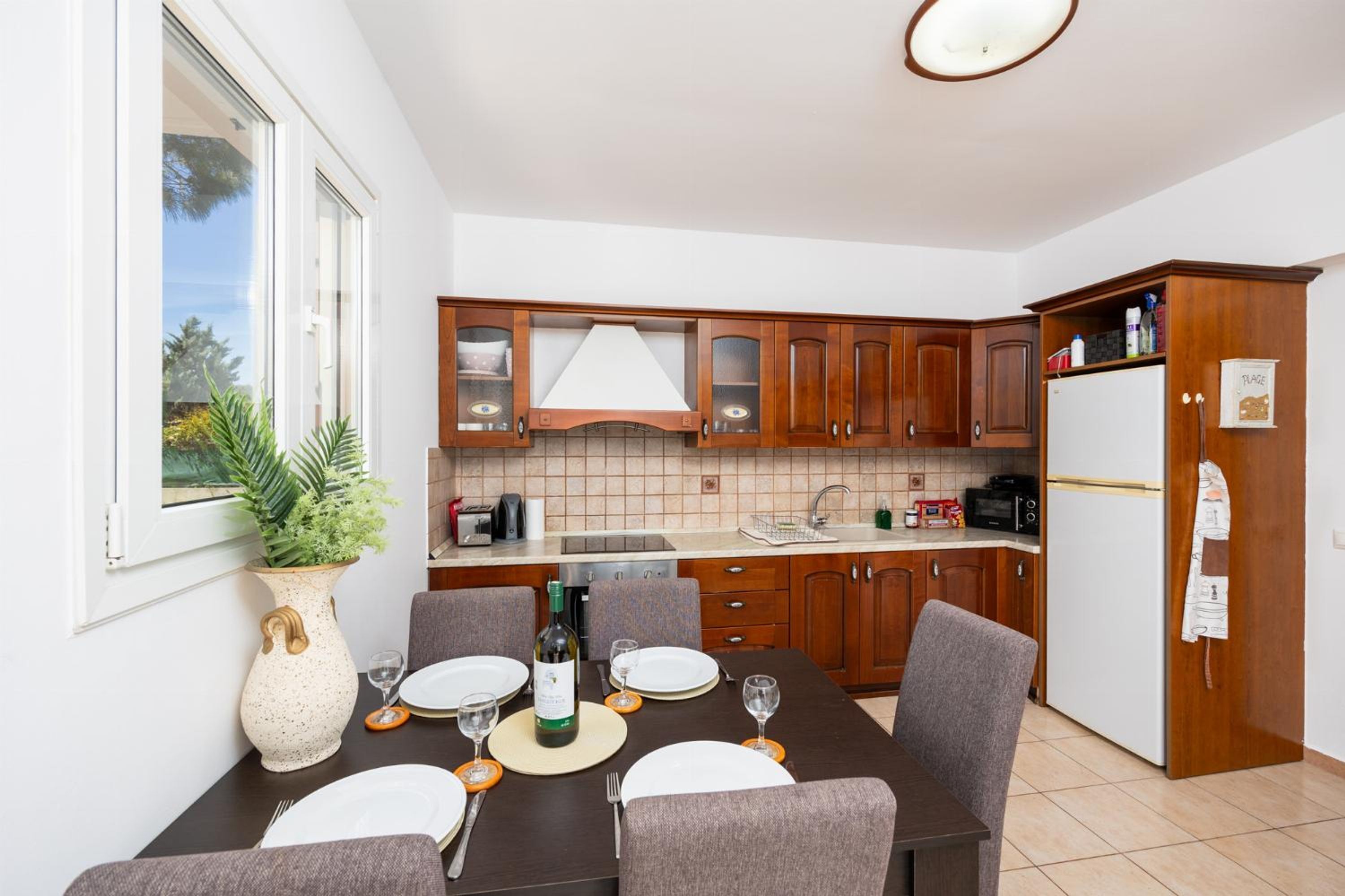 A modern kitchen with wooden cabinets, a dining table set for four, and a refrigerator.