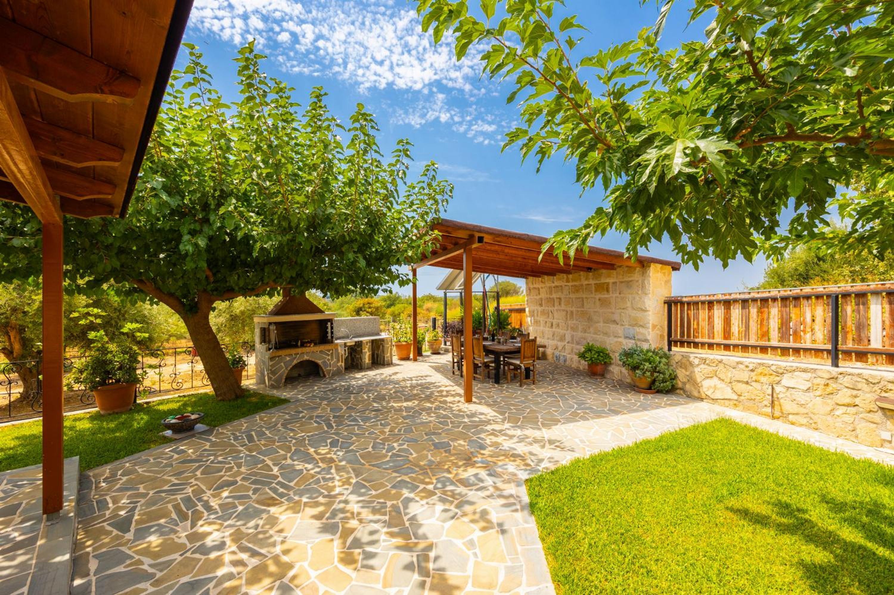 Eine Außenpatio mit Steinboden, einem Grill und einer Sitzecke unter einer Holzpergola.