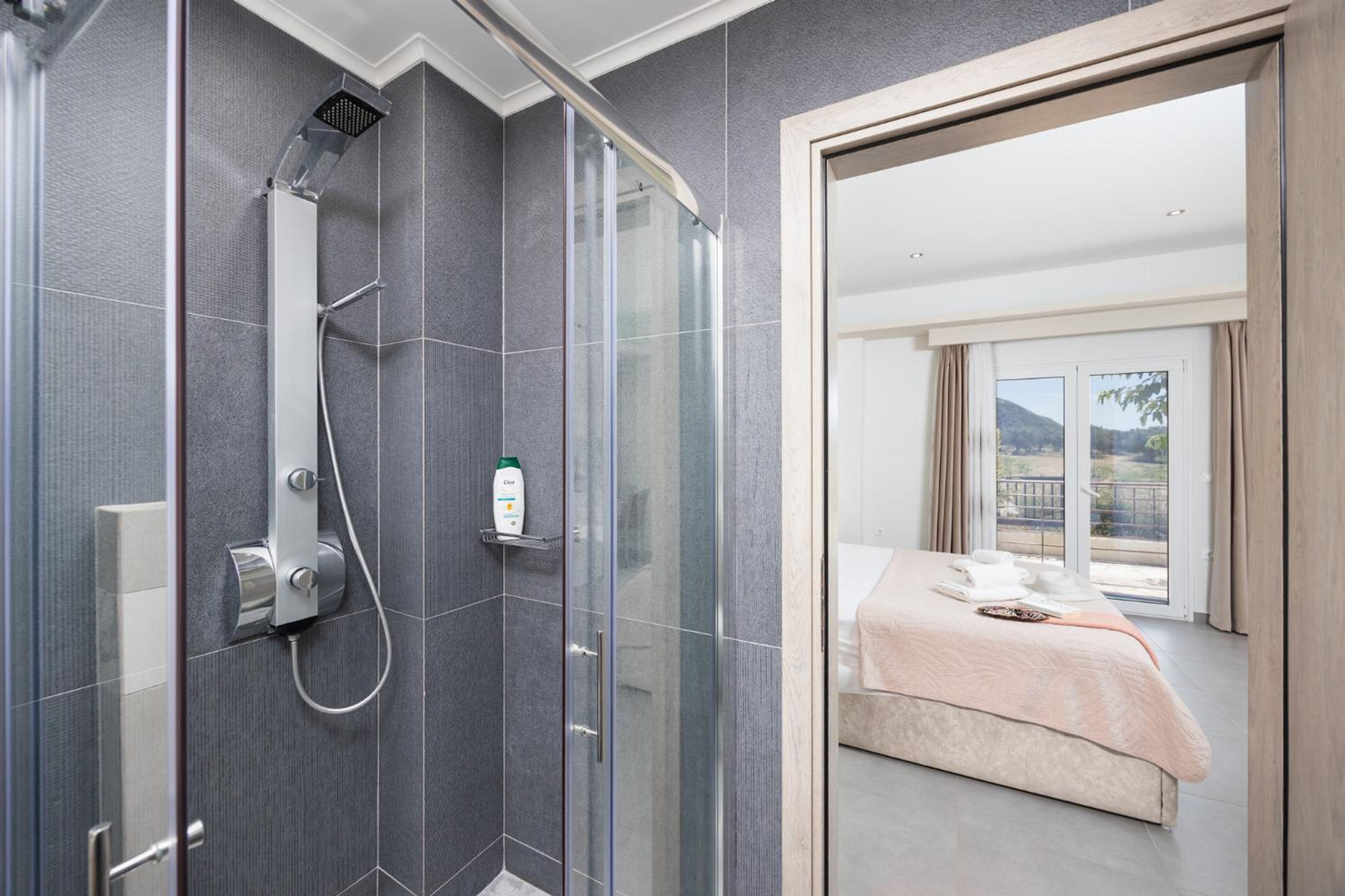 Un bagno moderno con doccia, una porta in vetro che conduce a una camera da letto con letto e vista.
