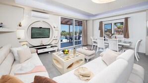 Un salón moderno con televisor de pantalla plana, comedor y balcón con vista a la piscina.