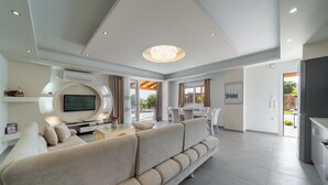 Una sala de estar moderna con un sofá grande, televisor y una zona de comedor con sillas y mesa.