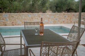 A poolside table with a bottle and glass, surrounded by wicker chairs. - Villa Castillo Ena in Agios Nikolaos (West Mani)
