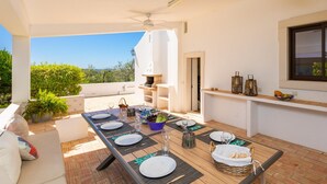 A covered outdoor dining area with a table set for four, a ceiling fan, and a stone oven. - Casa do Carmo in Moncarapacho (Olhao)