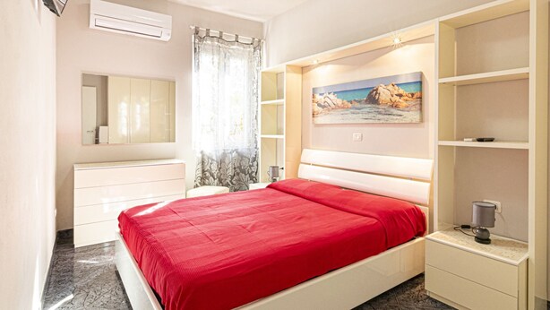 Une chambre à coucher avec un lit, une table de chevet, un miroir, une étagère et un tableau accroché au mur.
