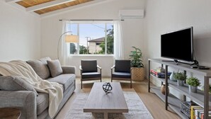 Ein modernes Wohnzimmer mit einer Couch, zwei Sesseln, einem Couchtisch, einem Fernseher und einem Bücherregal.