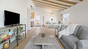 Ein modernes Wohnzimmer mit Flachbildfernseher, einem grauen Sofa, einem Holztisch und einem Bücherregal mit Pflanzen.