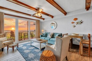 A room with a balcony, a ceiling fan, a sofa, a coffee table, and a dining table.