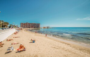 A beach with people sunbathing and swimming. There is a large building in the background. - Nice home in Torrevieja with swimming pool (Torrevieja)
