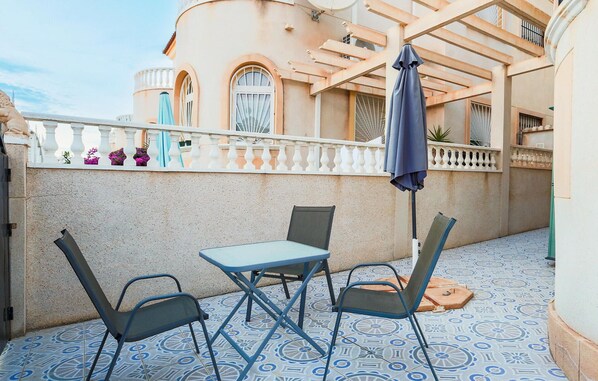 An outdoor patio with a table and two chairs, a blue umbrella, and a patterned floor. - Nice home in Torrevieja with swimming pool (Torrevieja)
