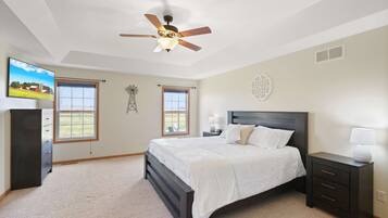 Une chambre à coucher comprenant un lit, une table de chevet, une commode, un ventilateur de plafond, deux fenêtres et une horloge murale.