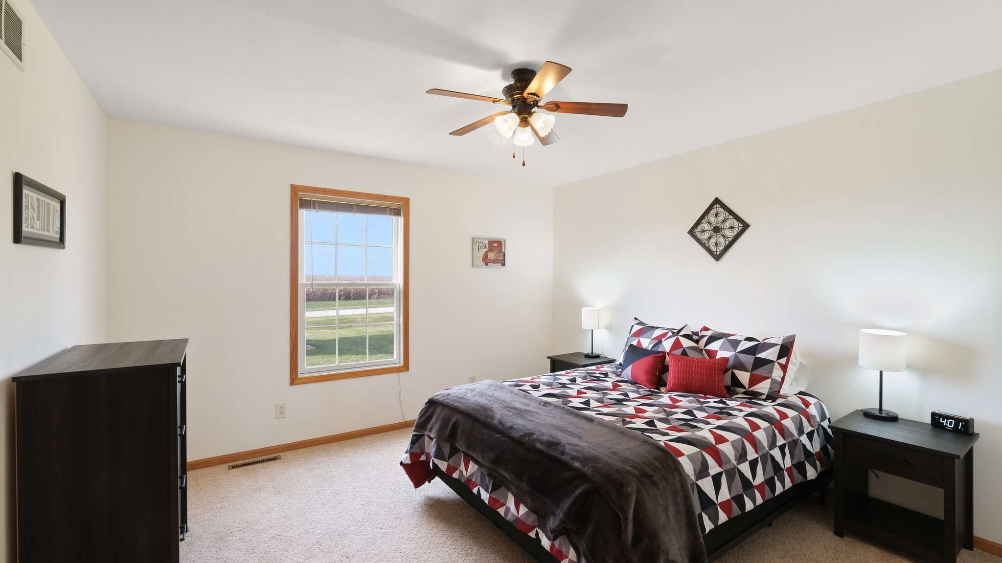 A bedroom with a bed, bedside tables, a ceiling fan, a window, and a wall clock.