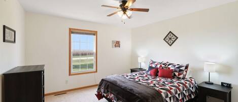 A bedroom with a bed, bedside tables, a ceiling fan, a window, and a wall clock.