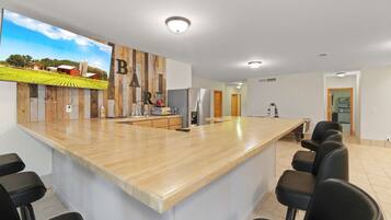 Une cuisine moderne avec un îlot central en bois, des tabourets de bar, un grand téléviseur et un réfrigérateur.