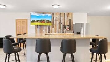 Une cuisine moderne avec un mur d’accent en bois, un grand îlot central doté de tabourets, un téléviseur encastré et un réfrigérateur.