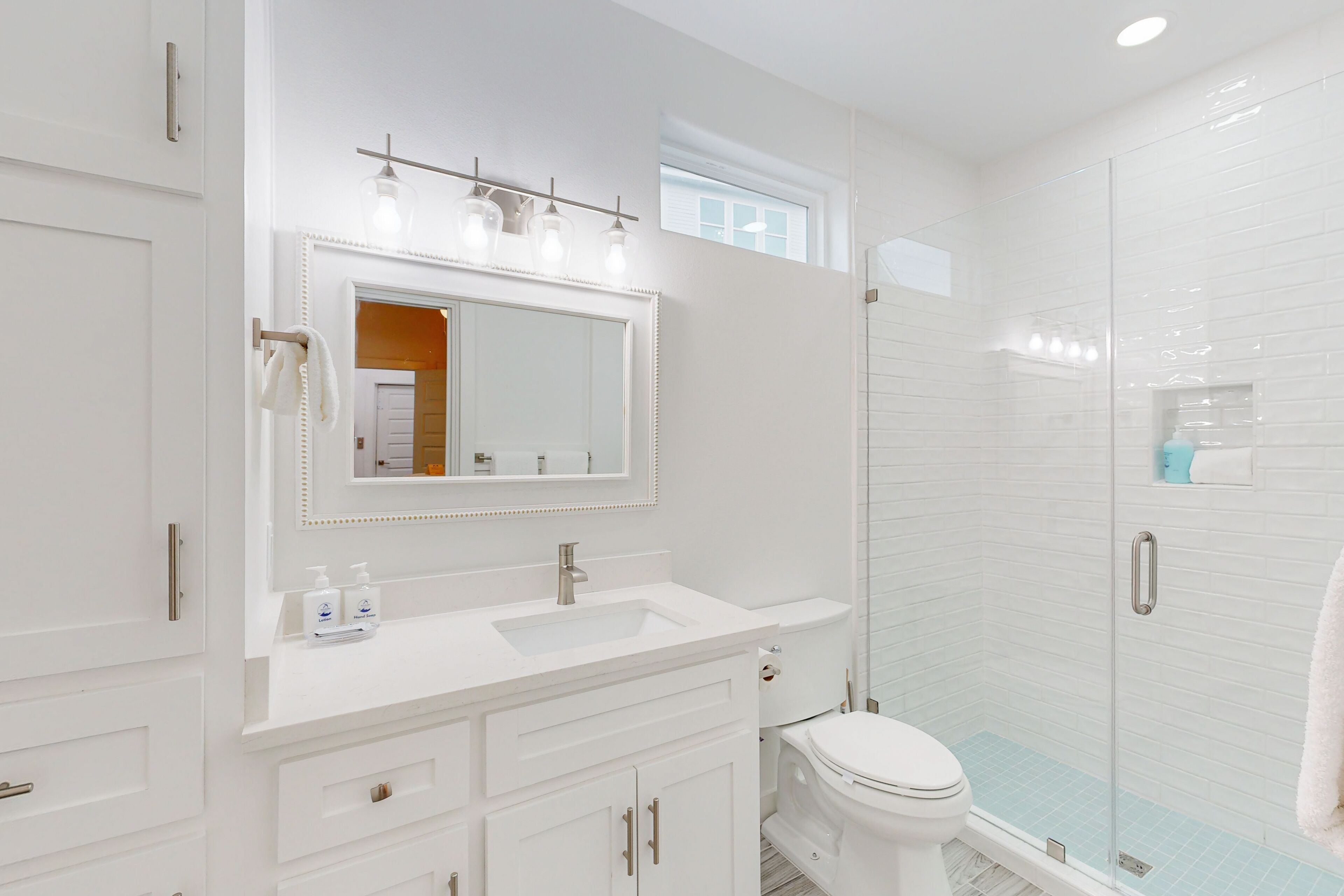 Un baño moderno con un espejo grande, tocador blanco y ducha con mampara de vidrio.
