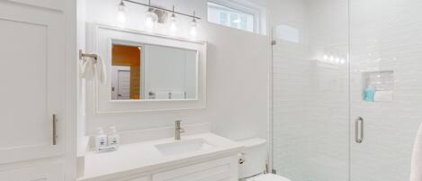 Un baño moderno con un espejo grande, tocador blanco y ducha con mampara de vidrio.