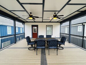 Ein überdachter Außenbereich mit Tisch und Stühlen, zwei Deckenventilatoren und einer Tür.